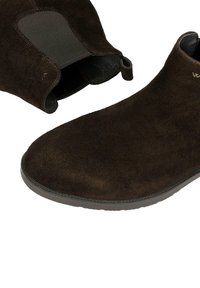 Brązowe zamszowe botki za kostkę z elastycznymi panelami po bokach, zaokrąglonym noskiem i kontrastowym przeszyciem; posiadają pętelkę ułatwiającą zakładanie.