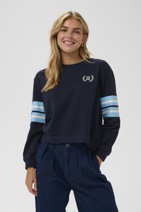 Jūras spēku pelēks krekls ar garām piedurknēm, kas ir ar trim gaiši ziliem svītrām katrā rokā. Mazs logotips uz krūtīm, kokvilnas un sintētisko šķiedru maisījums, īsā dizainā.