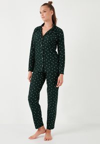 Ensemble de pyjama vert comprenant un haut à boutons et un pantalon assorti, tous deux ornés de motifs d'étoiles blanches et d'une texture douce et lisse.