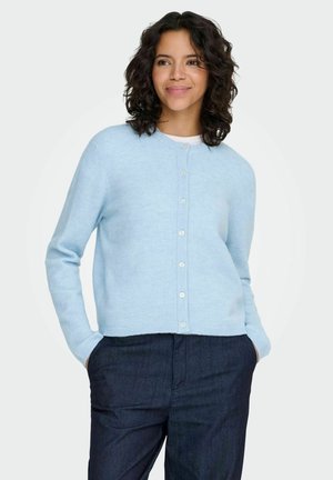 Hellblauer Strickcardigan mit Rundhalsausschnitt, Knopfleiste und gerippten Ärmelbündchen. Wird über dunkelblauen Jeanshosen mit weitem Schnitt getragen.