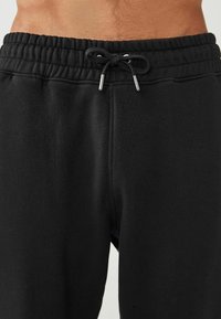 Pantalones de chándal negros con cintura elástica y cordón. Fabricados con material suave, de textura lisa y sin patrones visibles.