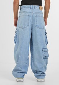 Lyseblå baggy cargo-jeans med store lommer, høy midje og en lærlabel. Designet med en avslappet passform og rett ben.