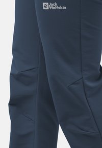 Pantalons de sport bleu marine en tissu doux, avec un design épuré, des poches zippées et un petit logo sur la cuisse.