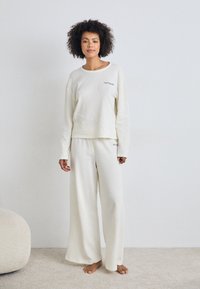 Conjunto de roupa de lounge branco e texturizado, composto por uma blusa de manga longa e calças largas. Detalhe bordado discreto no peito. Ajuste suave e descontraído.