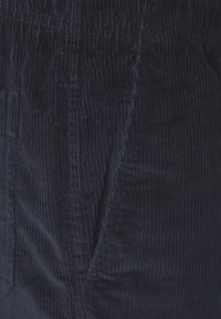 Marineblauwe corduroy broek met verticale ribbeltextuur, voorzien van zijzakken en een elastische tailleband voor comfort en gemak bij het dragen.