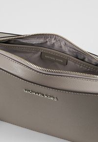 Monedero con cremallera de Michael Kors en suave piel color taupe, con un exterior texturizado, hardware plateado y una etiqueta con el logo en el interior.