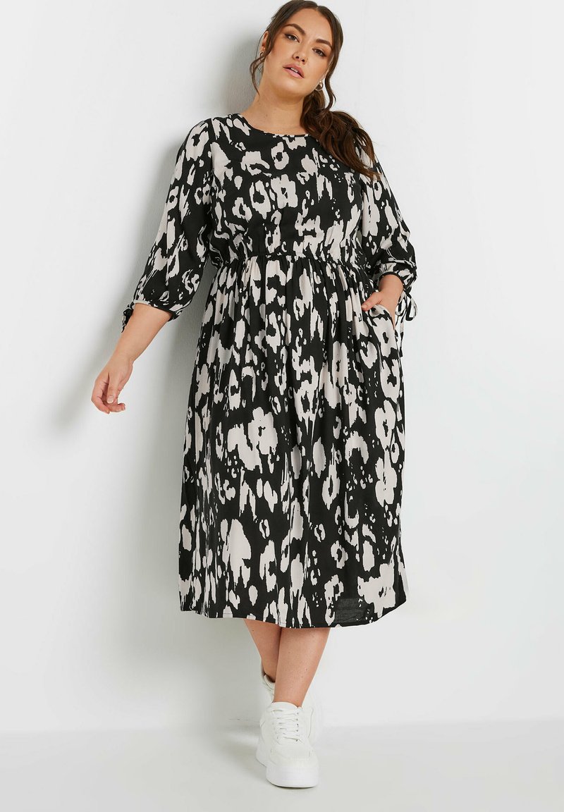 Svart och gräddfärgad leopardmönstrad midiklänning med trekvartsärmar, elastisk midja, sidofickor och en flödande kjol, i kombination med vita sneakers.