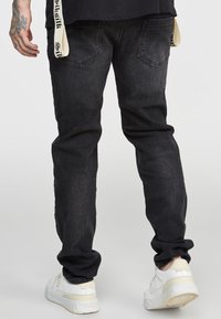 Svarta denimjeans med avsmalnande passform, som har fem fickor, subtila slitningar och en märkt rem vid midjan. Avslutas med vita sneakers.