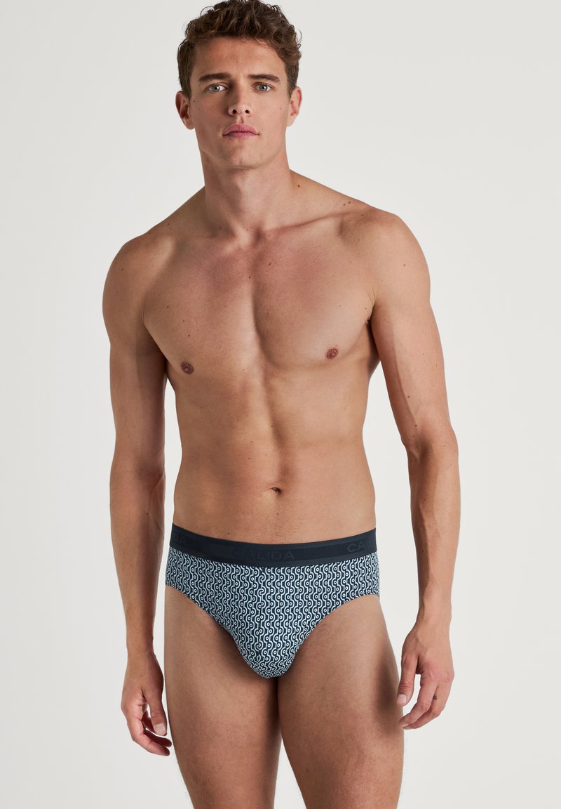 Herenboxers in een marine patroon met witte krullen. De tailleband is effen marineblauw met ingedrukte merknaam. Gemaakt van rekbare stof.