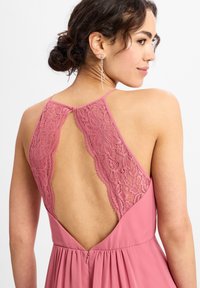 Rotes Kleid mit einem Spitzenrückendesign, verstellbaren Trägern und einem fließenden Rock. Details umfassen einen V-förmigen Rücken und einen Reißverschluss.