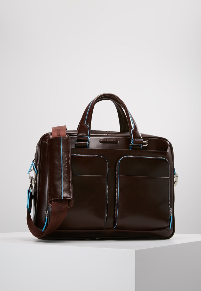 Borsa in pelle marrone con accenti blu, dotata di due tasche frontali e una tracolla rimovibile. Texture liscia e forma strutturata.