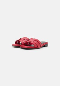 Sandales à glissière en cuir rouge avec un petit talon noir, présentant des détails de design découpés et une texture lisse sur la partie supérieure.