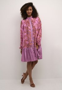 Dlhé rukávy, ružové šaty s kvetinovým vzorom, gombíkový predný diel, volánový golier a textúrovaný tierový lem. Hladká tkanina, voľný strih.