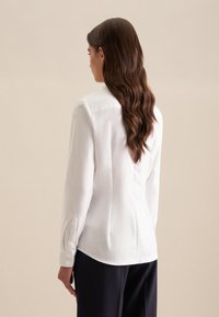 Witte blouse met lange mouwen en een getailleerde pasvorm, met een rechte achternaad, knopenmanchetten en een gladde stofstructuur. Combinatie met donkere broek.