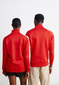 Røde zip-sweatshirts med høje kraver, ribstrikkede manchetter og kant. Enkelt tekstur, tætsiddende design og kontrastfarvede hvide sidestreger.