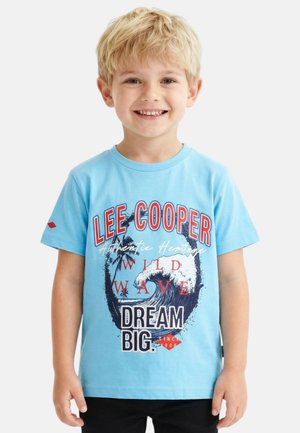 Jeune garçon blond souriant, portant un t-shirt bleu clair avec un motif de vague et le texte « LEE COOPER WILD WAVE DREAM BIG ».