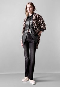 Kardigan s leopardím vzorem přes černou koženou košili, doplněný tmavými džínami a bílými teniskami. Má strukturované látky a volný střih.