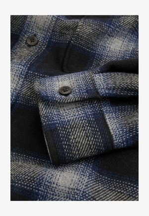 Material în carouri albastre și gri, cu o textură moale, două nasturi negri și un guler pliat cu un model în carouri.