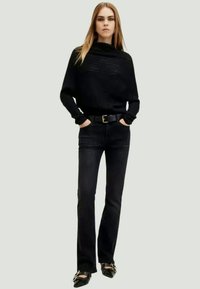 Μαύρο πλεκτό πουλόβερ με σχέδιο ζακέτας, με οριζόντιες ρίγες, συνδυασμένο με σκούρες τζιν ψηλόμεσες παντελόνες και μαύρες γόβες με αγκράφες.