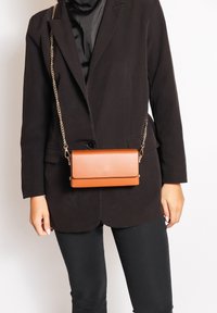 Borsa a tracolla in faux leather marrone con tracolla a catena; forma rettangolare, texture liscia e chiusura a scatto con design minimalista.