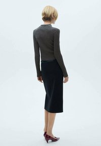 Smal figursyet, ribbet mørkegrå sweater med krave, parret med en knælængde sort nederdel. Modellen bærer blanke burgunderhæle.