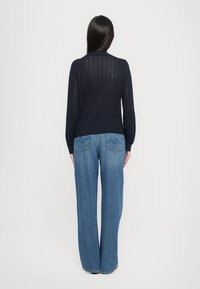 Tumesinine kootud sviiter avatud õmblusmustriga, koos kõrge vöökohtadega laia jala siniste teksadega, millel on dekoratiivsed tagataskud.