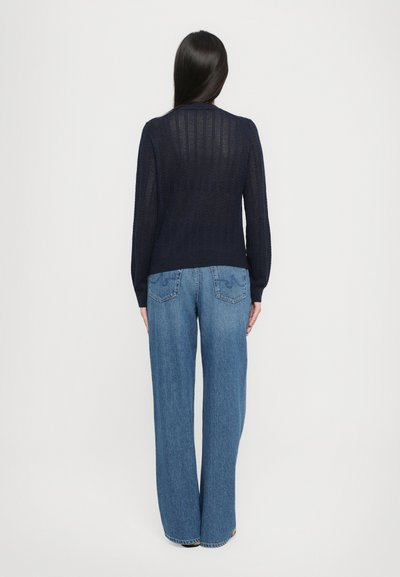 Jūras spēku zila adīta džemperis ar atvērtu šuvju rakstu, kombinēts ar augstām, platām zilo džinsu biksēm ar dekoratīvām aizmugures kabatām.