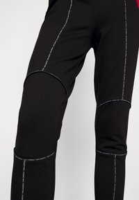 Zwarte sportbroeken met contrasterende stiksels en gebogen kniestukken. Gemaakt van een gestructureerde stof met accenten van het merkembleem aan de zijkanten.