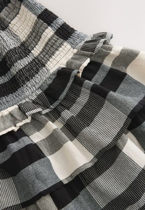 Raukšlėtas audinys su juoda, balta ir pilka languota rašte, puoštas rauktais detalėmis ant tekstūruotos medžiagos.