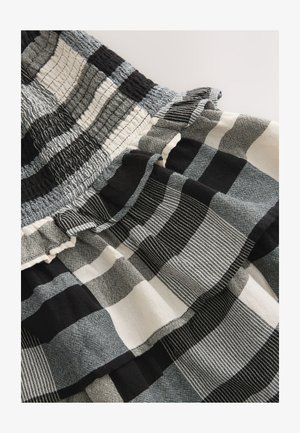 Kortsudunud kangas musta, valge ja halli ruudulise mustriga, millel on volditud detailid tekstuuriga materjalil.