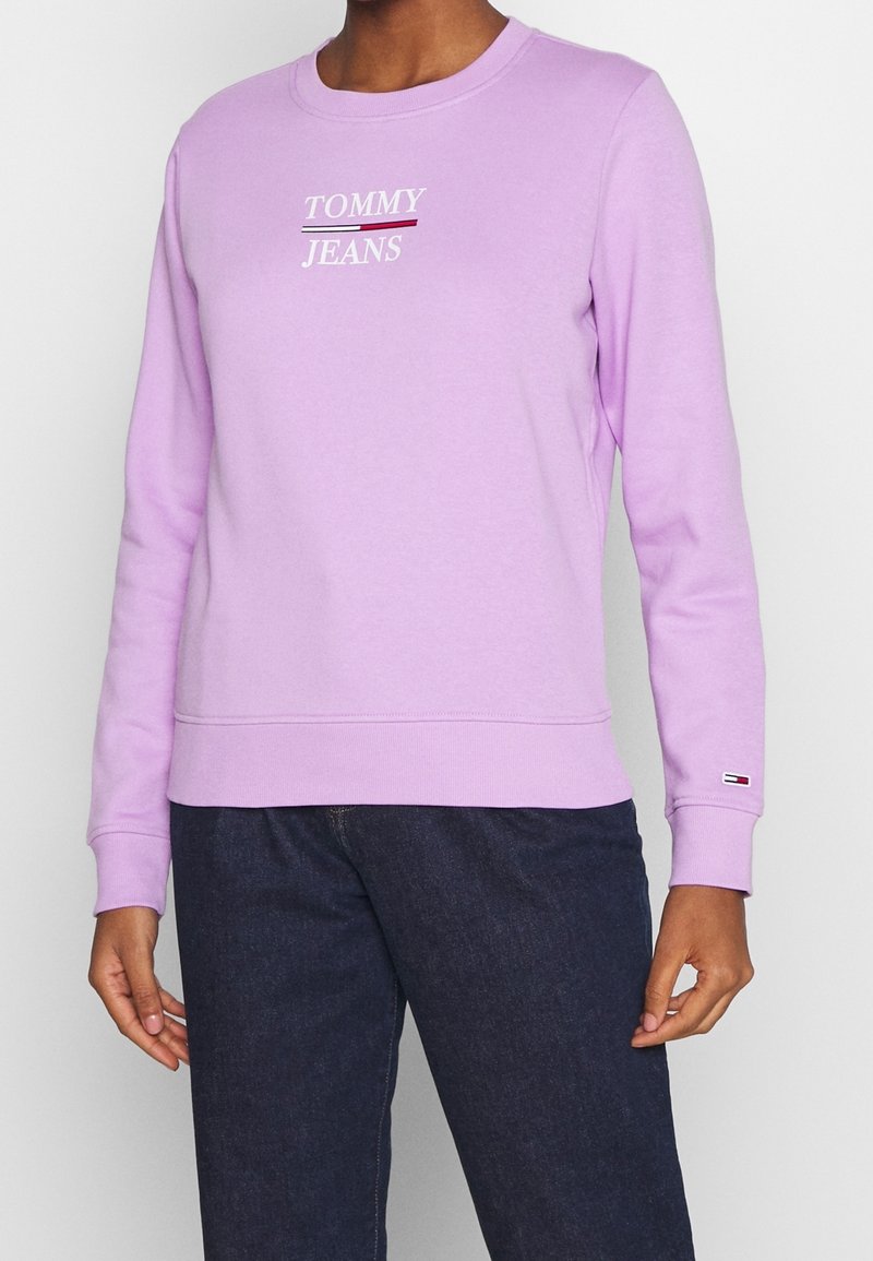 Lila bomulls sweatshirts med rund hals, prydd med vit och burgundy texten "TOMMY JEANS" över bröstet och ribbad mudd.