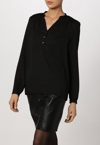 Czarna bluzka z długim rękawem wykonana z gładkiej tkaniny, z dekoltem w serek, trzema guzikami i delikatnymi marszczeniami na ramionach.