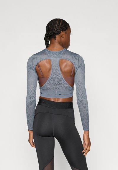 Μπλούζα άθλησης μακρυμάνικη σε ανοιχτό μπλε με υφασμάτινο μοτίβο, σχέδιο με ανοιχτή πλάτη και ρυθμιζόμενους ιμάντες πάνω από καφέ αθλητικό σουτιέν. Μαύρο κολάν.