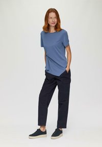 Blauwe kortekraagshirt met een gebogen zoom en zijknopen, gecombineerd met zwarte cargobroek en zwarte sneakers met een gestructureerde zool.