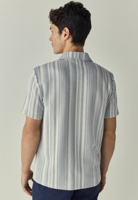 Chemise à manches courtes à rayures blanches et bleues, en tissu texturé. Présente un col et une coupe droite à l'ourlet.