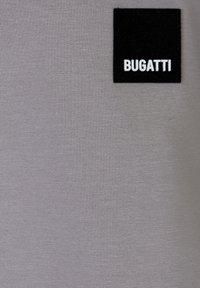 Tessuto grigio con una superficie liscia, caratterizzato da un'etichetta quadrata nera. L'etichetta presenta in modo evidente il testo bianco "BUGATTI".