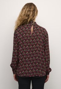Bluza s dugim rukavima od tamnosmeđeg tkanja s ružičastim i krem cvjetnim uzorkom, s detaljem u obliku ključa na leđima i dugmadi na manžetama.