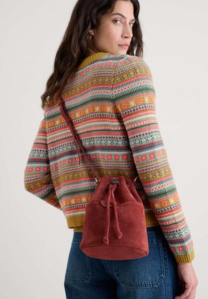 Rød ruskinds spandetaske med snørrelukning, parret med en flerfarvet mønstrede sweater og blå jeans. Har en skulderrem.