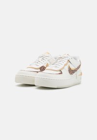 Sneakers bianchi in pelle con dettagli leopardati, suola testurizzata e branding arancione, caratterizzati da un design low-top e chiusura con lacci.