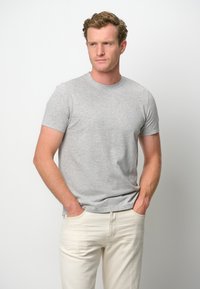 Grå bomullströja med rund halsringning och korta ärmar, tillsammans med ljusa denimjeans. Enkelt mönster, inga synliga mönster.