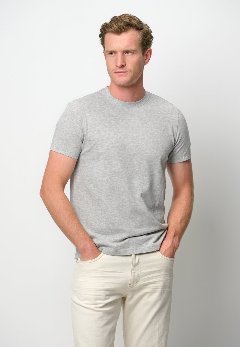 Grå bomullströja med rund halsringning och korta ärmar, tillsammans med ljusa denimjeans. Enkelt mönster, inga synliga mönster.