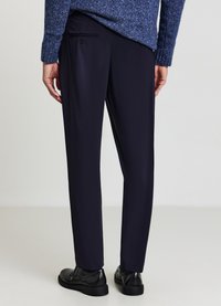 Pantalon marine ajusté, avec une poche arrière boutonnée, confectionné dans un tissu lisse et assorti à des chaussures noires.
