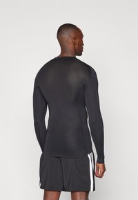 Langærmet sort træningsskjorte lavet af et struktureret, strækbart materiale, med rund hals og tætsiddende design, båret med sorte shorts.
