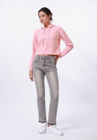 Felpa corta rosa con un motivo a spina di pesce testurizzato, abbinata a jeans grigi sbiaditi e sneakers bianche, su uno sfondo semplice.
