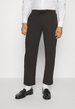 Dark brown sweatpants with a drawstring waistband, straight leg design, and vertical stitch details, paired with black loafers and white socks.