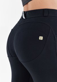 Leggings neri elasticizzati con un design aderente, texture liscia e un piccolo logo sulla tasca posteriore.