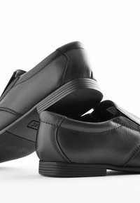 Zapatos de cuero negro con una textura suave, diseño sencillo, tacón bajo y sutiles acentos de costura, con suela de goma para mayor agarre.