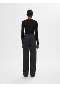 Sort langærmet top parret med højtaljede, brede mørk denimjeans med opfoldede manchetter og to baglommer. Simpelt design, glat texture.