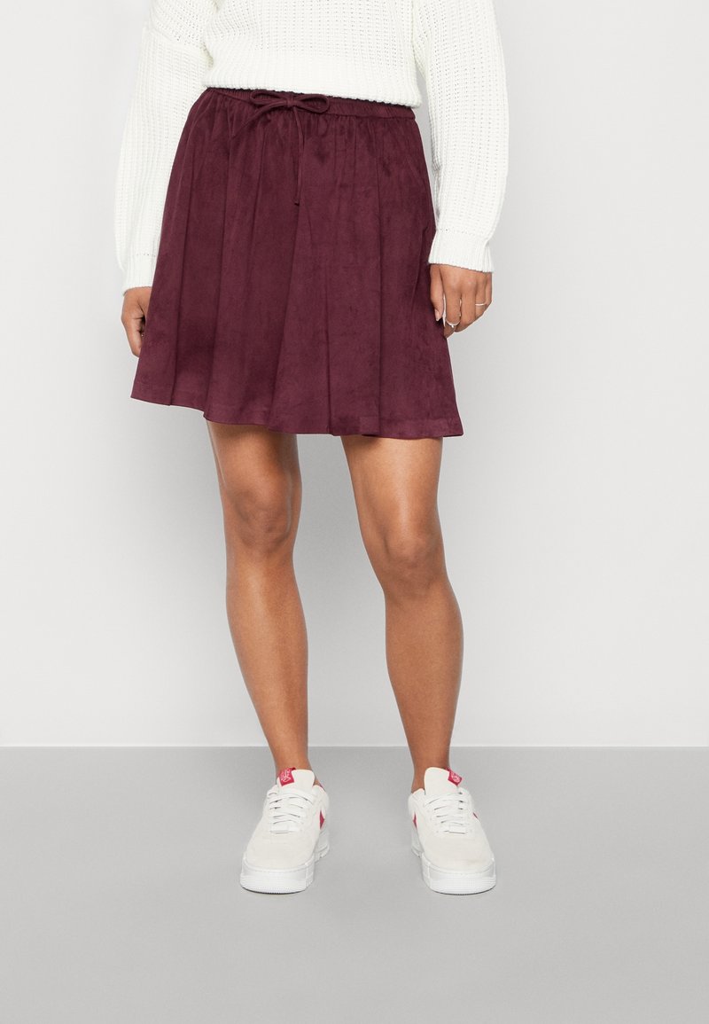 Jupe en daim bordeaux avec une coupe décontractée, dotée d'une taille à cordon de serrage et d'un design plissé, assortie à des baskets blanches.
