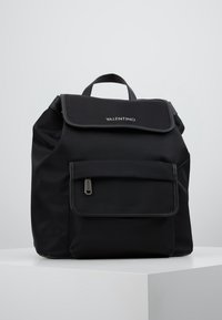 Black nylon backpack with a flat top flap, front zip pocket, and a logo. Features a fabric texture and dual adjustable shoulder straps.